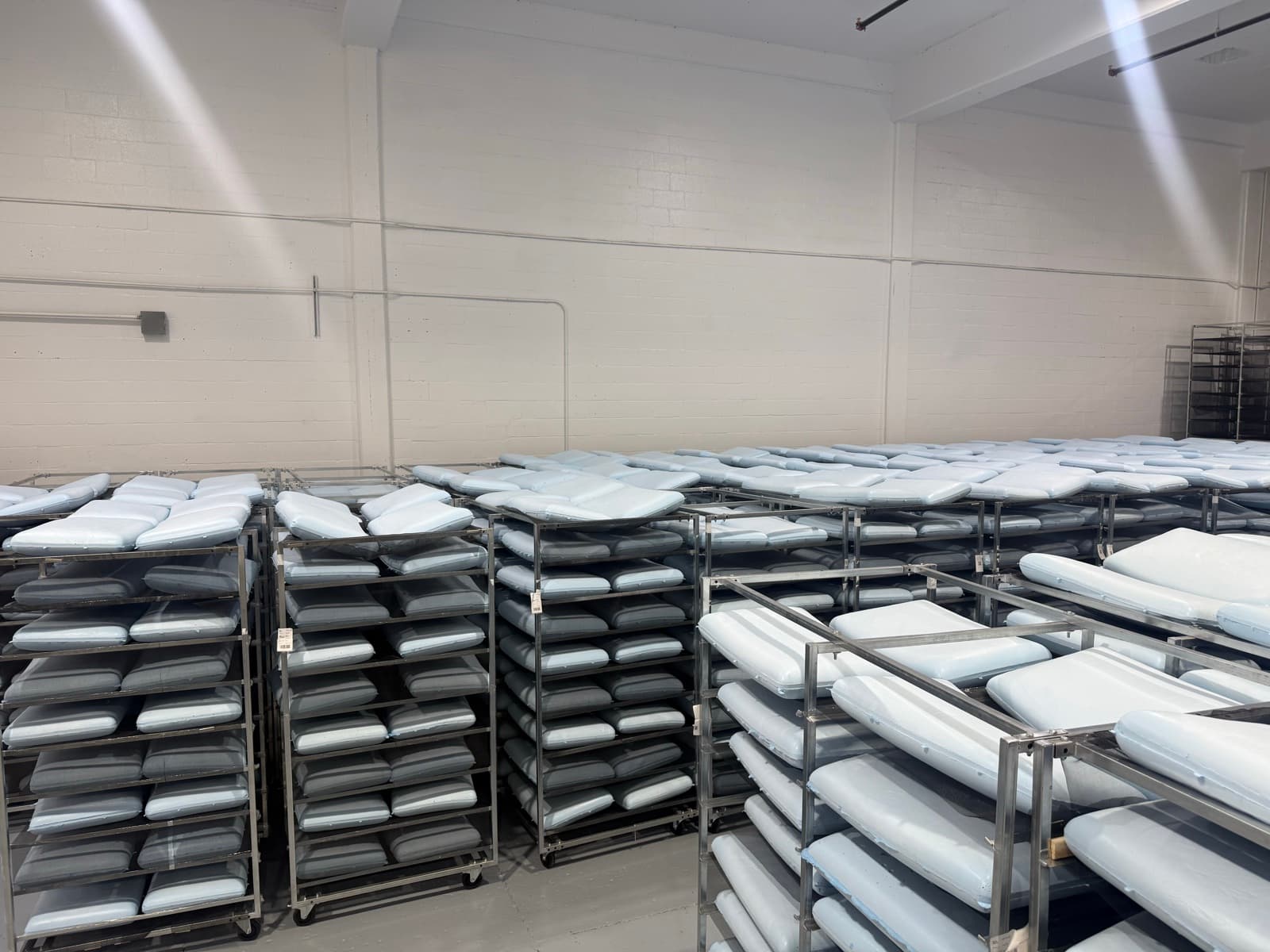 Rows of stacked memory-foam pillows on metal racks during the curing stage at the Maple Sleep factory.